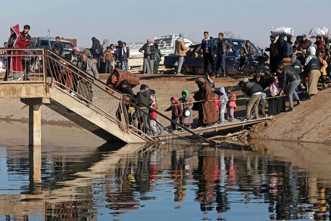 TOPSHOT - People along with their belongings walk across a damaged bridge as they flee from a Kurdish-controlled area, in Rasm al-Harmal, east of Aleppo city on January 15, 2026. Syrians began fleeing an area east of Aleppo city on January 15 after the army gave civilians a deadline to leave amid fears of an escalation in clashes with Kurdish forces. The government is seeking to extend its authority across the country following the ouster of longtime leader Bashar al-Assad a year ago. (Photo by Bakr ALKASEM / AFP)
