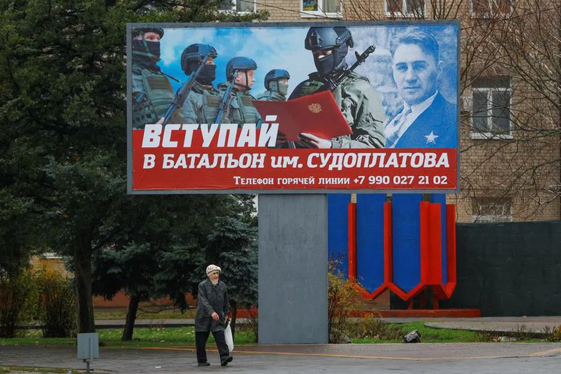 FILE PHOTO: A local resident walks past a board encouraging to join a Russian army battalion in the course of Russia-Ukraine conflict in Melitopol, Russian-controlled Ukraine, November 27, 2022. A slogan on the board reads: \"Join battalion named after Sudoplatov\". REUTERS/Alexander Ermochenko/File Photo