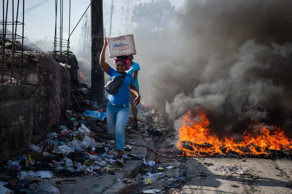 People walking past burning tires during a demonstration against insecurity in Port-au-Prince, Haiti, Aug 19, 2024. Haiti's prime minister escaped unharmed Monday after gangs opened fire near a hospital he was visiting, a government source told AFP, as the troubled nation seeks to restore stability after months of gang related violence.