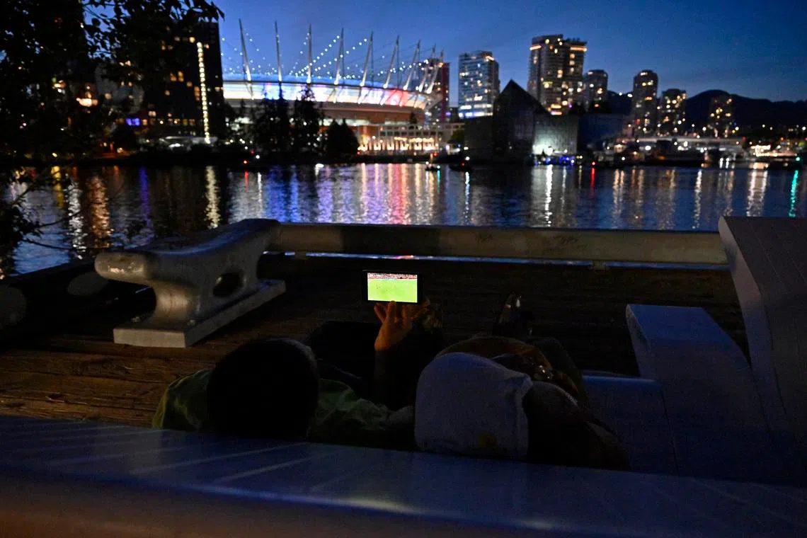 Soccer Football - FIFA World Cup 2026 - Group D - Australia v Turkey - Fans gather in Vancouver - Vancouver, Canada - June 13, 2026 A couple watches the match on their phone near the BC Place stadium REUTERS/Jennifer Gauthier