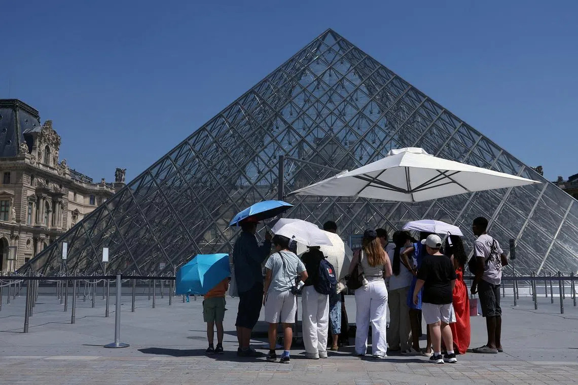 Tourists stand under umbrellas to protect themselves from the sun in front of the glass Pyramid of the Louvre museum as the museum closes early due to the heatwave as temperatures rise in Paris, France, June 24, 2026. REUTERS/Alice Sacco