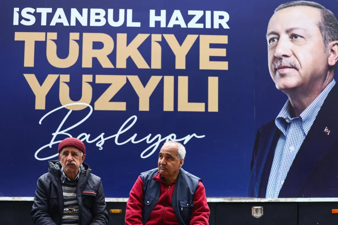 Two men sit in front of a campaign billboard in Istanbul featuring a photo of Turkish President Recep Tayyip Erdogan.
