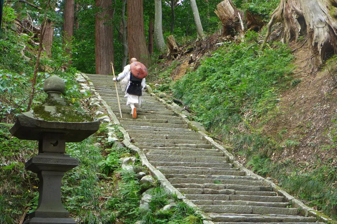 A white-robed priest walks up 2,466 steps to a Shinto shrine complex atop Mount Haguro, Japan.