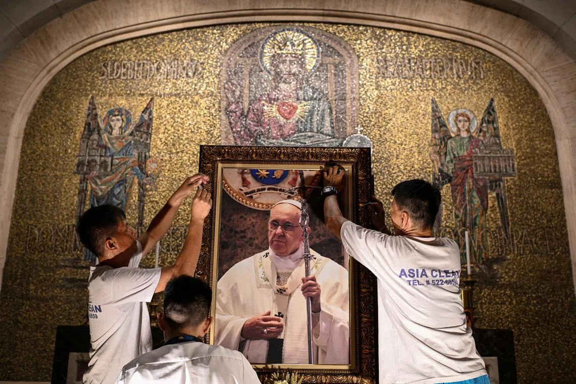Church workers attach a picture of Pope Francis aftrer his death announced by the Vatican, at the Manila Cathedral, Philippines, April 21, 2025. REUTERS/Noel Celis