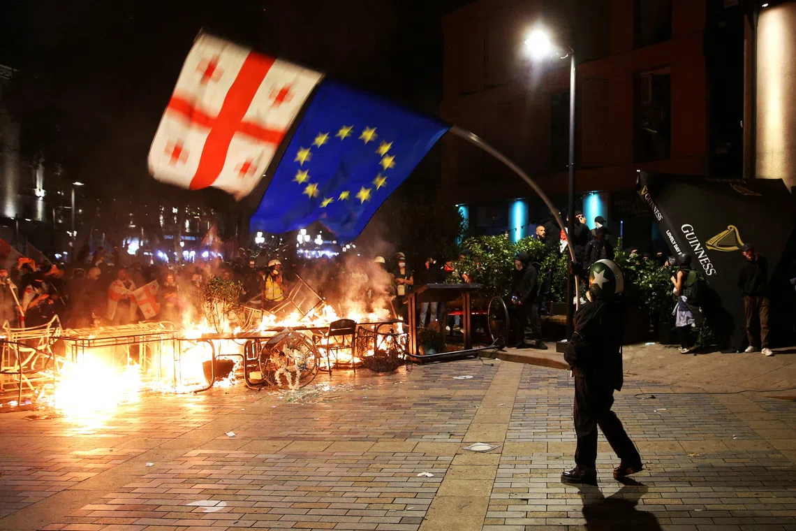 FILE PHOTO: A protester waves Georgian and EU flags in front of a burning barricade during an opposition rally on the day of local elections in Tbilisi, Georgia October 4, 2025. REUTERS/Irakli Gedenidze/File Photo