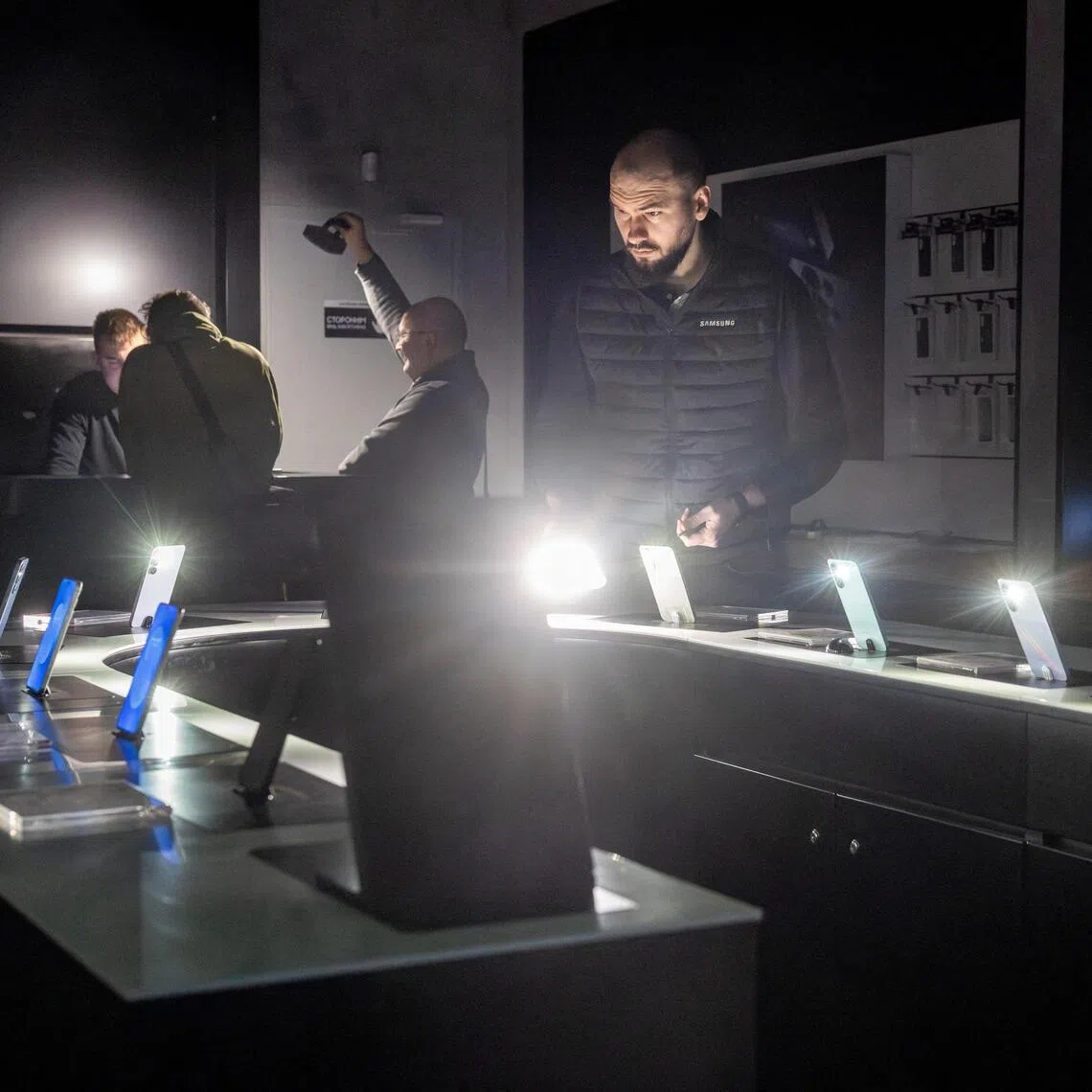 A shop assistant turning on the flashlights of smartphones at a mobile phone shop in Kharkiv, Ukraine, during the electricity blackout on Jan 31.