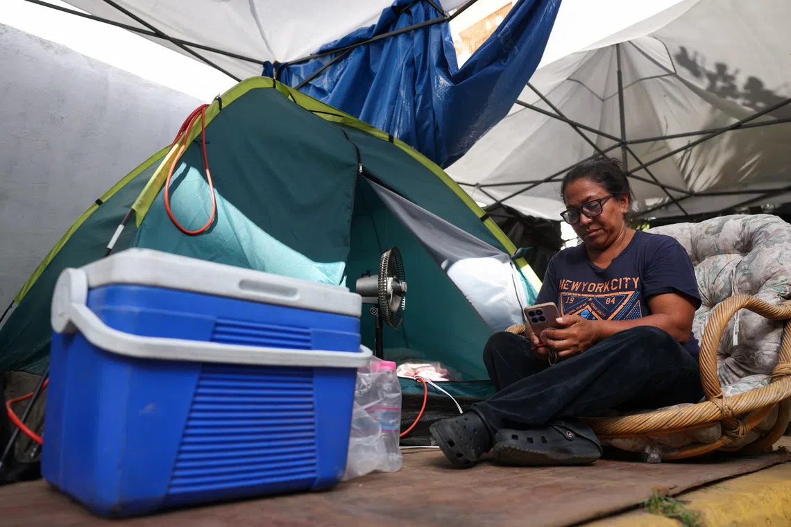 A woman uses her phone while sitting next to a tent where she sleeps after her building collapsed, as Venezuelans face worsening power and water shortages following government warnings of drought linked to the El Nino phenomenon, deepening hardships for a population already coping with daily outages and the aftermath of devastating earthquakes, in La Guaira, Venezuela, August 7, 2026. REUTERS/Leonardo Fernandez Viloria