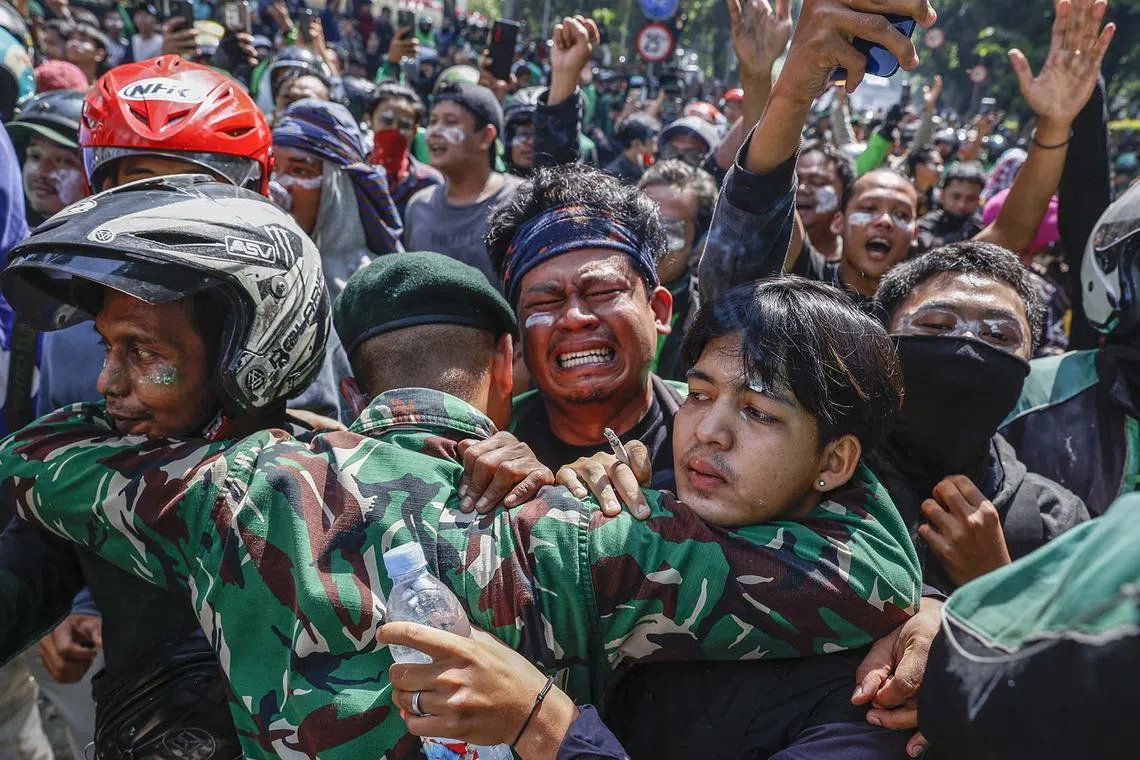 A protester wiping tears as he is comforted by military personnel after clashing with police outside the Mobile Brigade Police headquarters in Jakarta, Indonesia, Aug 29, 2025. Hundreds of protesters and motorbike-hailing drivers staged a protest following the death of a motorbike-hailing driver during an earlier demonstration against the housing allowance for members of parliament. 