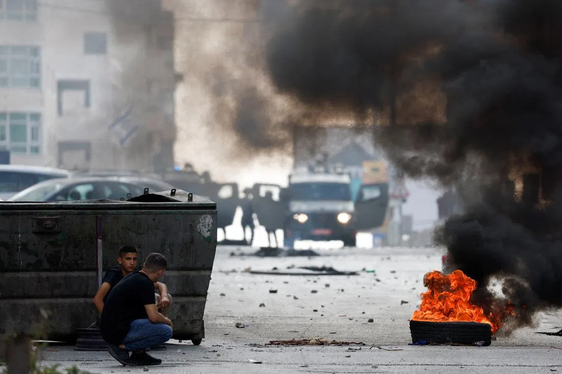 Israeli soldiers stand next to military vehicles as Palestinians cover near a burning tire during an Israeli raid in Qalandya, in the Israeli-occupied West Bank, October 7, 2024. REUTERS/MohamadTorokman