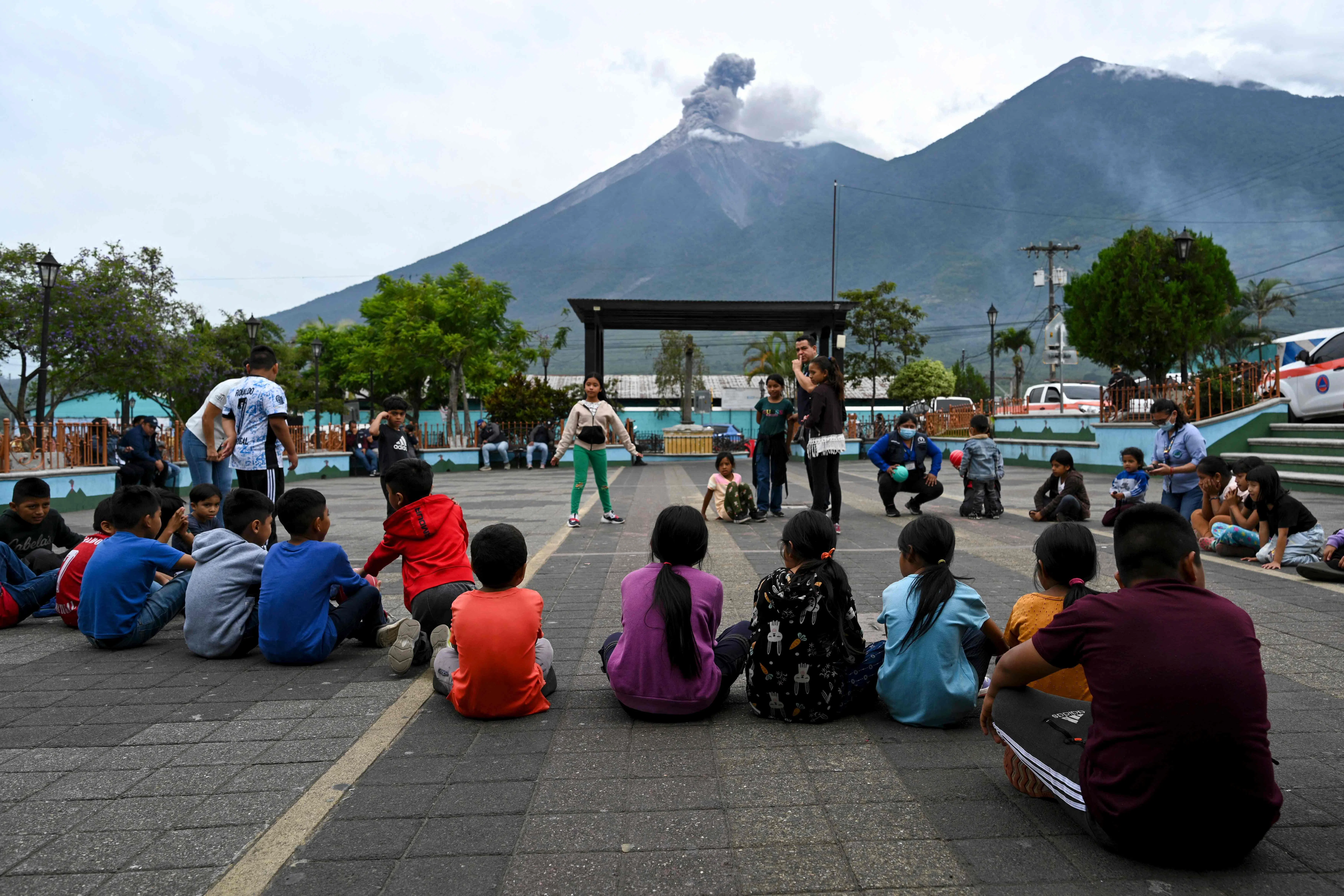 Children gathered at a town square on Aug 4, as Guatemala’s Fuego volcano erupts in the distance.