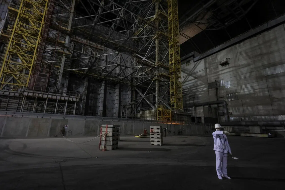 An employee measures a radiation level next to the old sarcophagus covering the damaged fourth reactor, under the New Safe Confinement (NSC) structure at the Chornobyl Nuclear Power Plant, amid Russia's attack on Ukraine, in Kyiv region, Ukraine April 22, 2026. REUTERS/Gleb Garanich