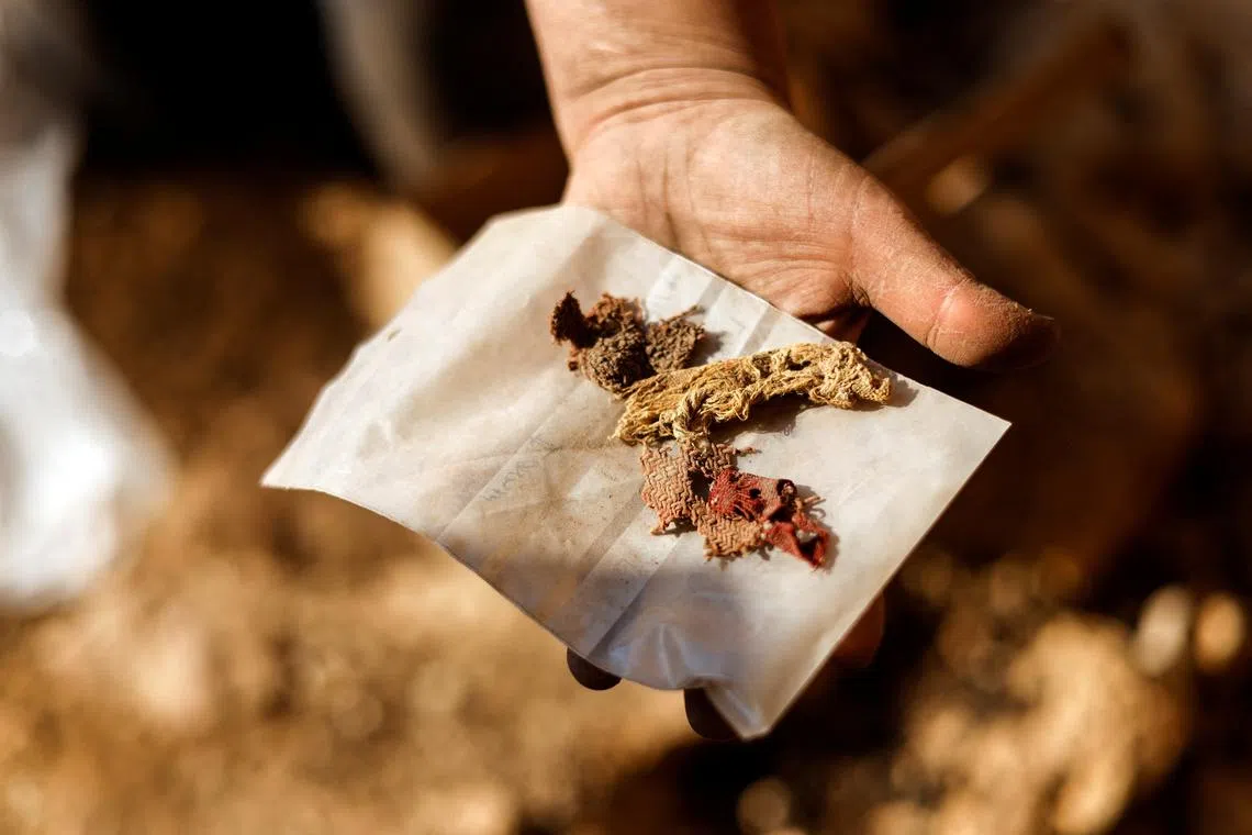 An excavator holds up pieces of cloth in a desert cliff excavation overseen by the Israel Antiquities Authority in Muraba'at Cave near the Dead Sea, in the Israeli-occupied West Bank December 28, 2022. 