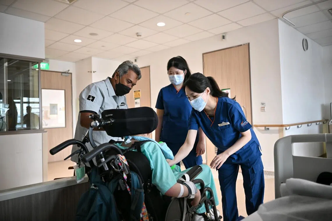 (Left) Mr Mohd Aszrin Ahmad, 51, and his son (seated) Dean Joaquim Mohd Aszrin, 14, with (centre)  physiotherapist Jilene Lau, and occupational therapist Yang Ching Wen, both from Sengkang Community Hospital, at the Paediatric Care ward.