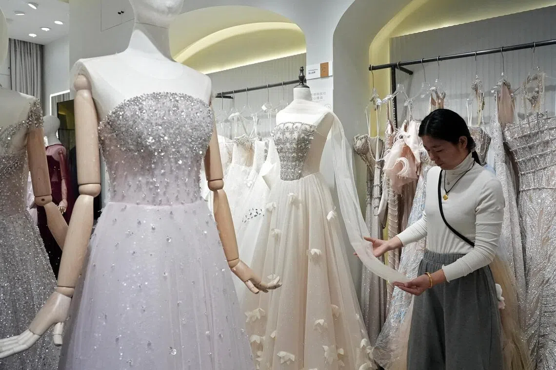 Wedding dress seller Zhu Jiaomei inspects a gown's fabric at Huqiu Bridal City in Suzhou, Jiangsu province, China January 16, 2026. REUTERS/Nicoco Chan