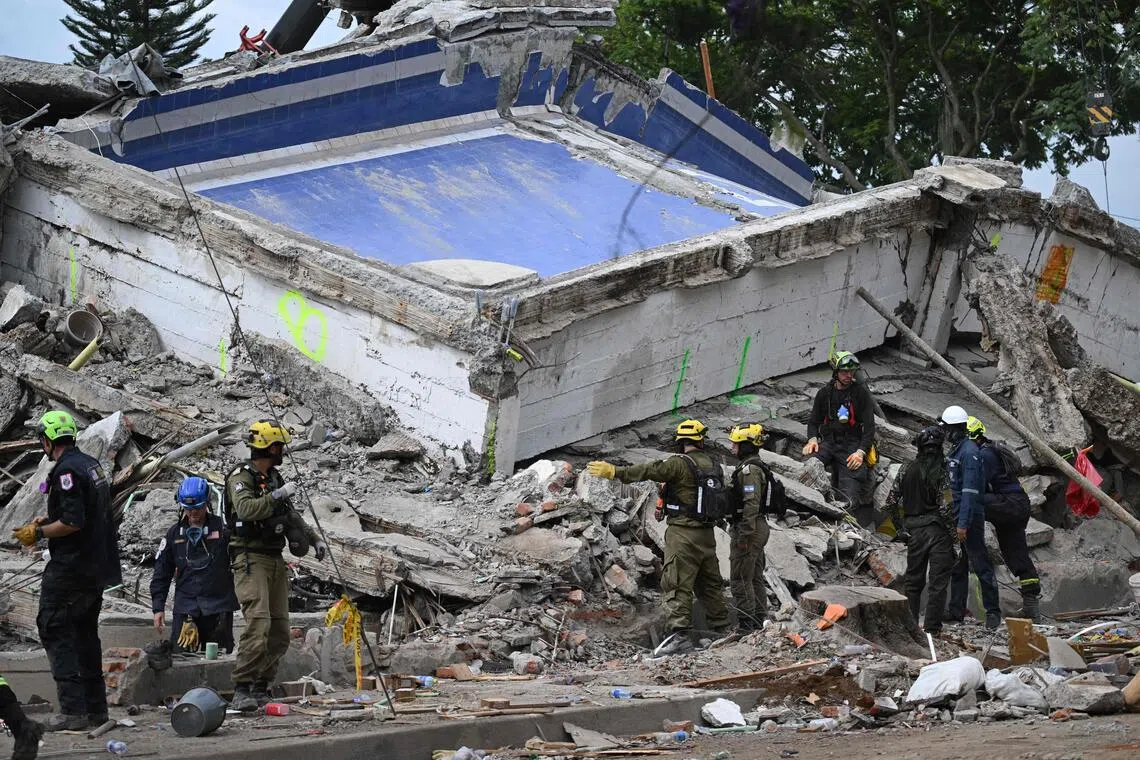 Rescuers in protective gear examine the rubble of a collapsed building.