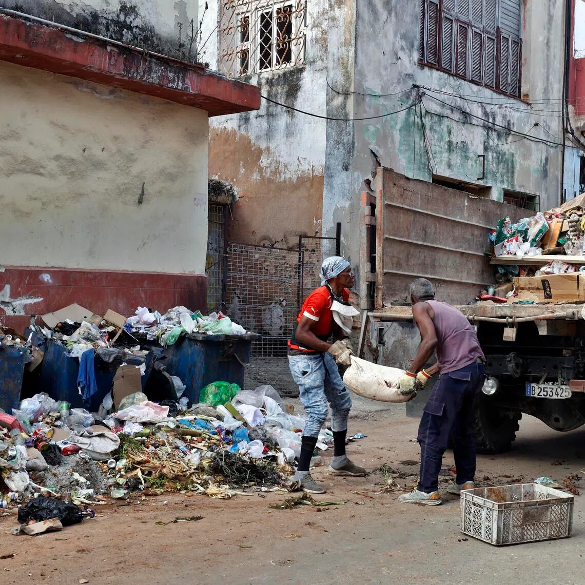 People collect trash on a street in Havana on March 5, 2026, as US energy blockade on Cuba imposed since January continues.