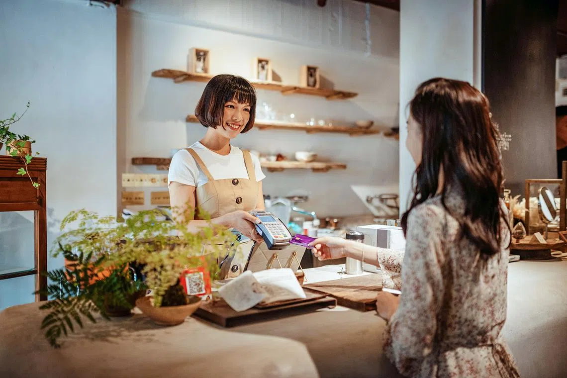 Asian woman cashier taking payment from a female shopper