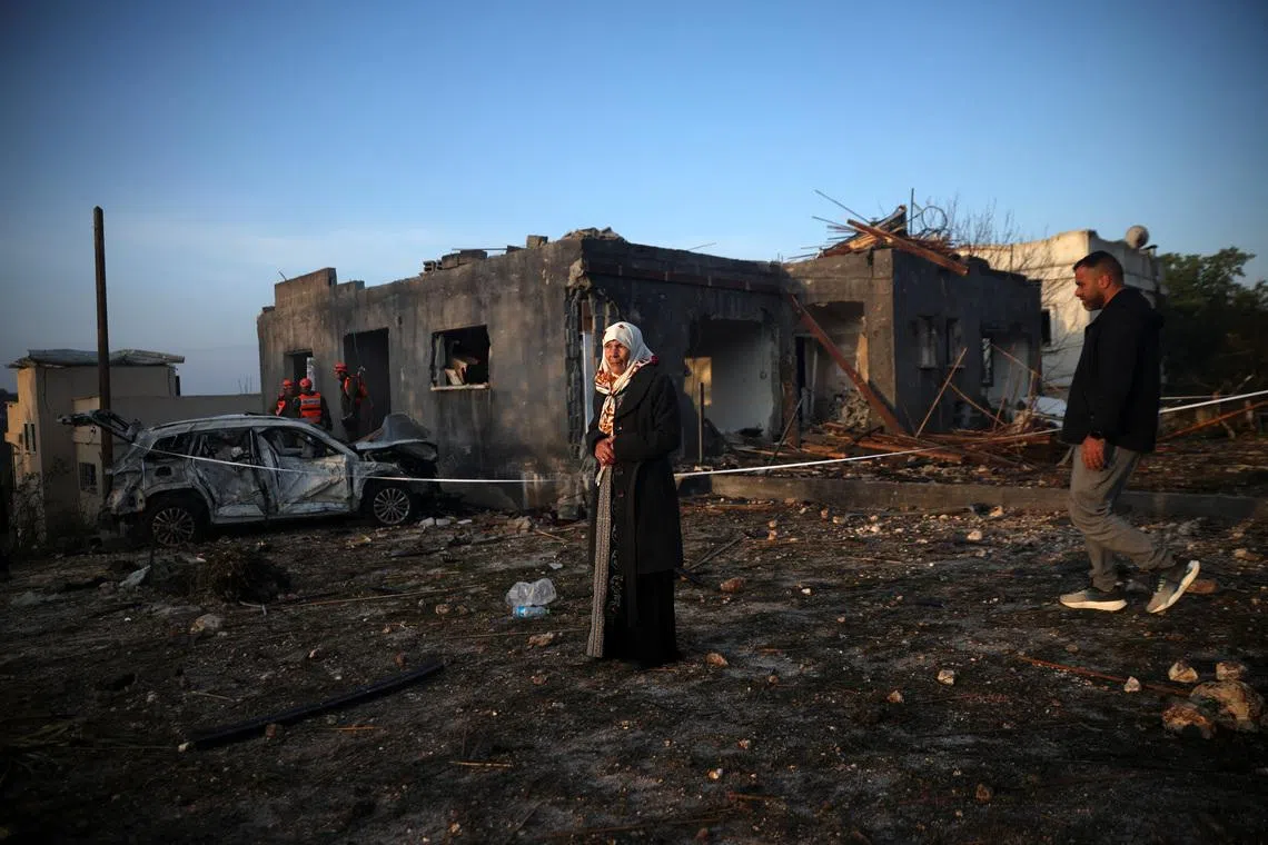 A woman stands as Israeli emergency responders work at the site of an impact by an Iranian missile, amid the U.S.-Israel conflict with Iran, in northern Israel, March 13, 2026. REUTERS/Shir Torem