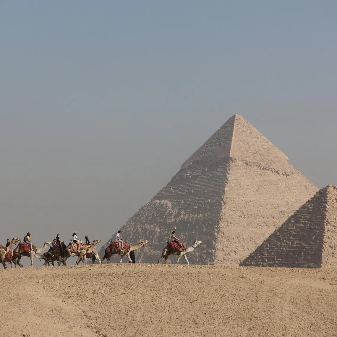 FILE PHOTO: Tourists ride camels in front of the Great Pyramids plateau in Giza, Egypt December 11, 2022. REUTERS/Amr Abdallah Dalsh/File Photo