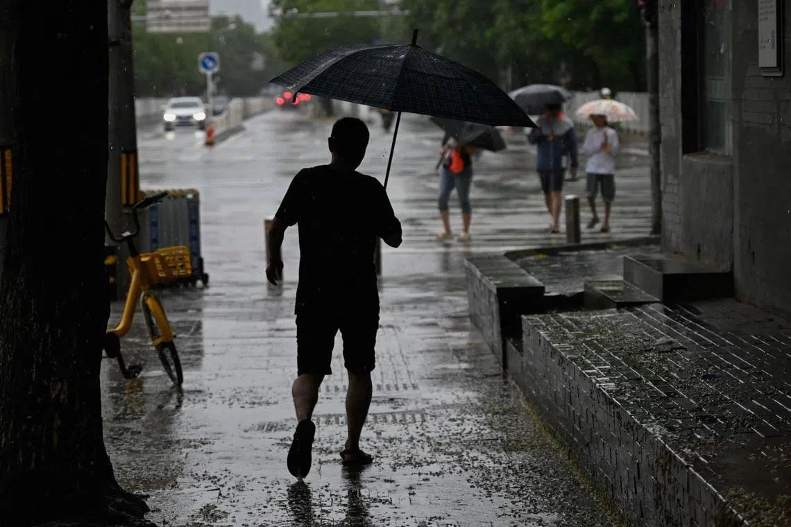 A man shelters from the rain with an umbrella in Beijing on July 30, 2023. China put a part of the north of the country on red alert, including the Beijing region, due to torrential rains expected from the advance of typhoon Doksuri, which is currently hitting the other end of the country. (Photo by Pedro PARDO / AFP)