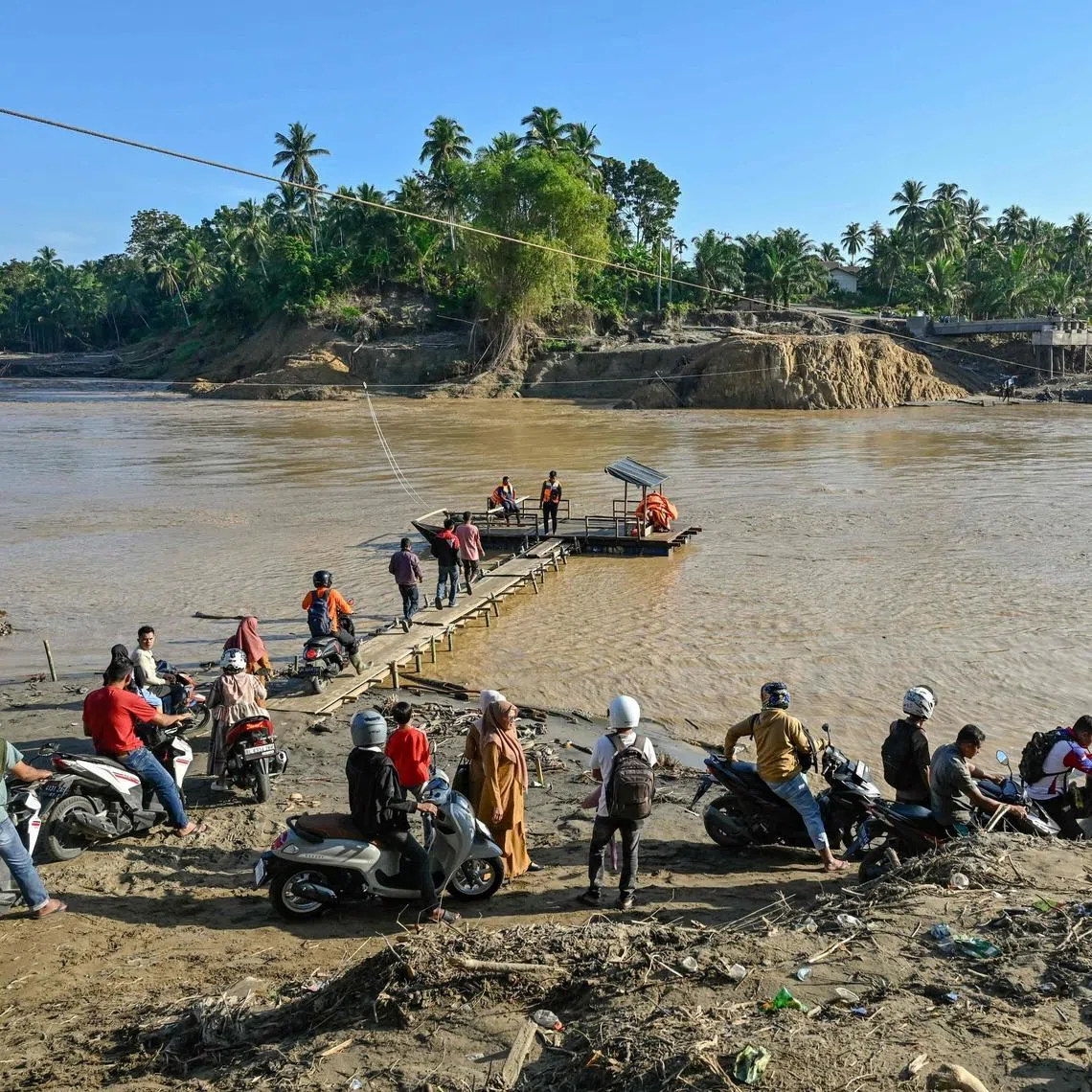 People waiting to cross a river following flash floods in Bireuen district, Aceh, on Jan 5. Heavy rain also triggered flash floods on the island of Siau.