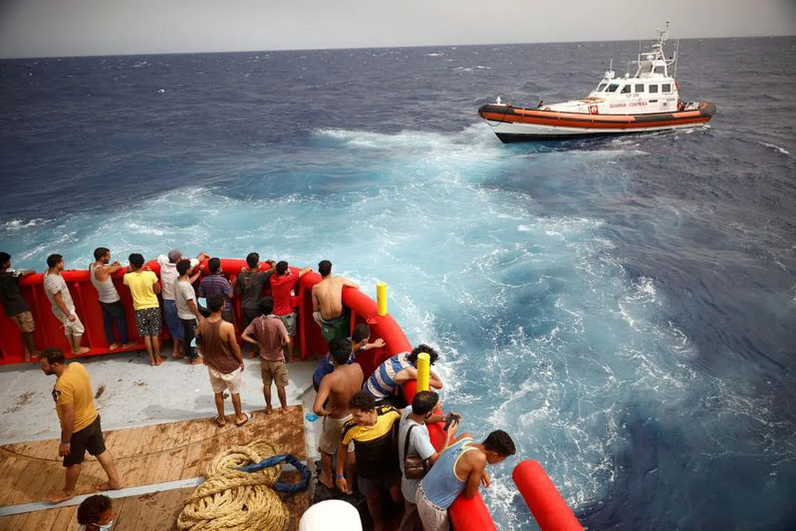 FILE PHOTO: Migrants on board of NGO Proactiva Open Arms Uno rescue boat looks at boat Guardia Costiera heading to Lampedusa island, in central Mediterranean Sea, close to Lampedusa island, Italy, August 19, 2022. REUTERS/Juan Medina/File Photo