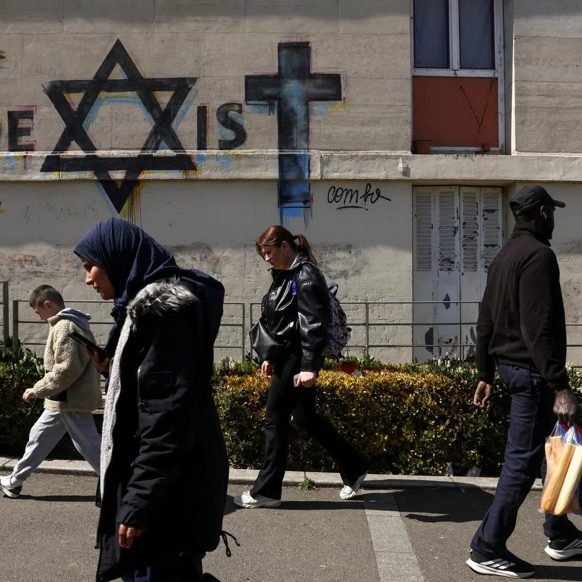 People walk past a mural which reads \"coexist\", made from religious symbols representing the religions of Islam, Judaism and Christianity, near to the market in the Paris suburb of Sarcelles, France, April 14, 2026. REUTERS/Tom Nicholson