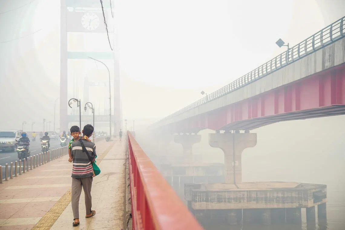 A man carrying a child walks along the Ampera Bridge in Palembang, South Sumatra on Oct 5 as haze from forest and land fires in the region blankets the sky and surrounding areas.