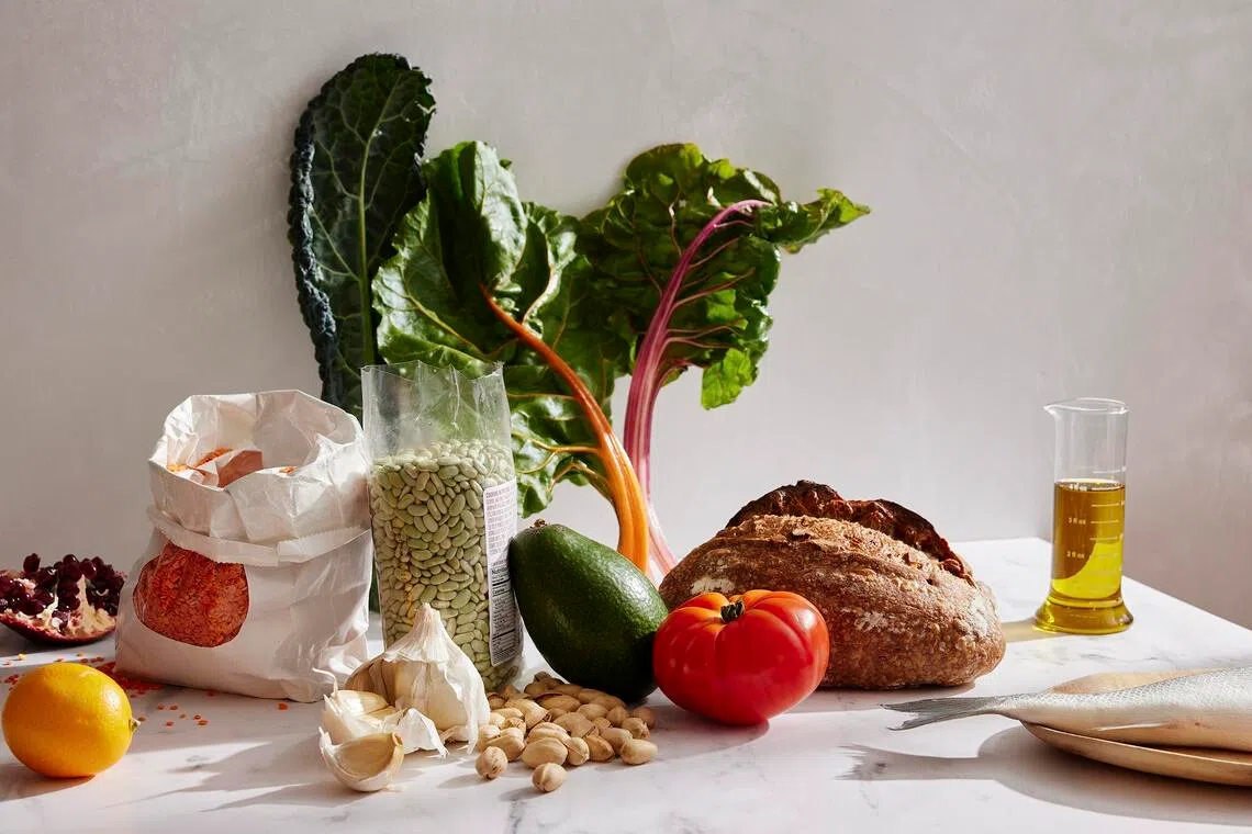 A variety of foods including tomato, pistachios, avocado, fish, bread and oil. 