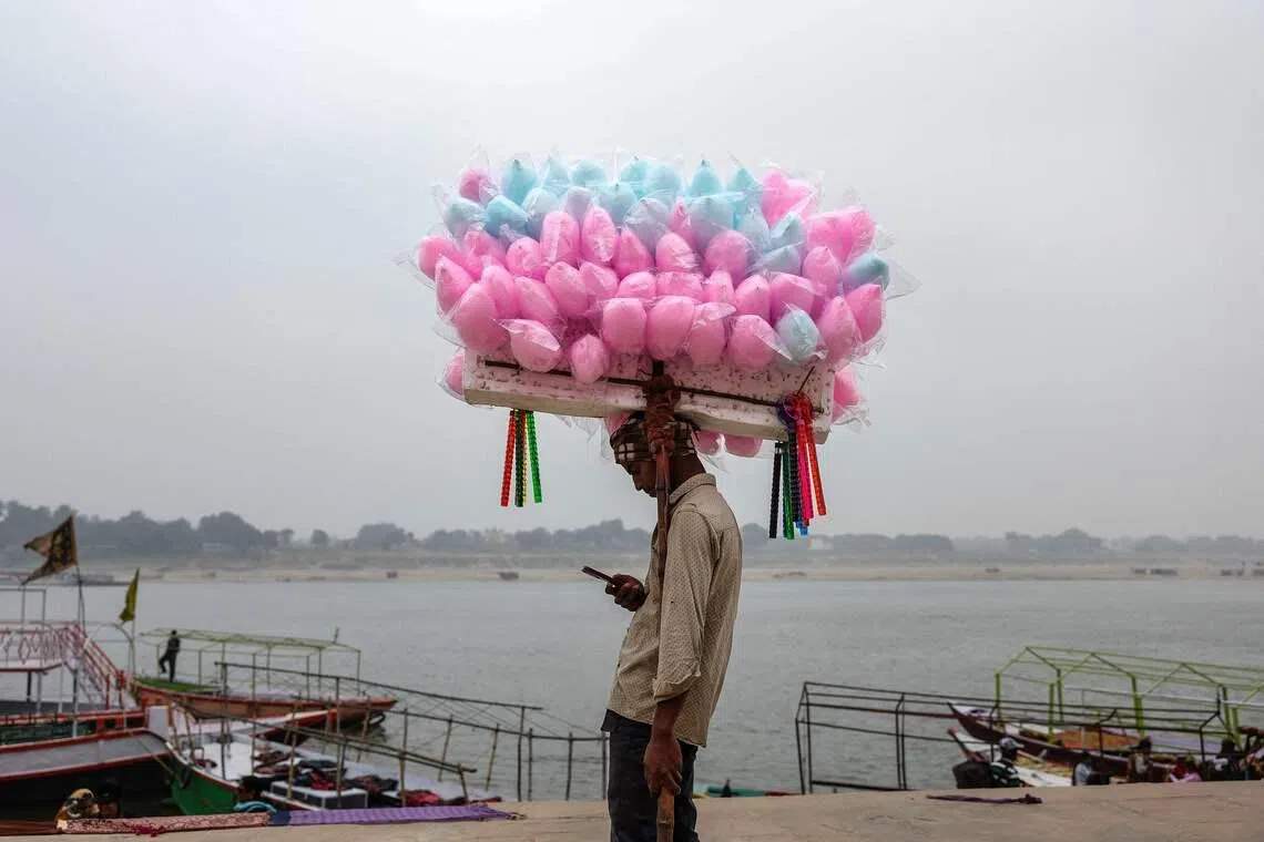 A cotton candy vendor taking a break and using his mobile phone as he waits for customers along the banks of the river Ganges in Varanasi, India on Jan 29, 2026. 