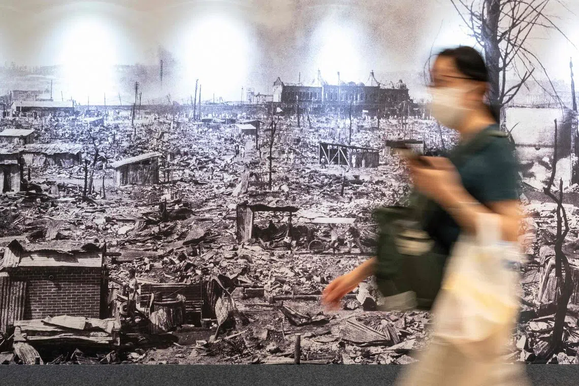 TOPSHOT - A woman walks past a photo exhibition put up along a public passageway in central Tokyo on August 18, 2023, to remember the 1923 earthquake which hit the capital and surrounding areas. September 1, 2023 will mark the 100th anniversary of when Tokyo, neighbouring Yokohama and surrounding areas were struck by a 7.9 magnitude quake that left more than 100,000 people dead, the majority of whom died in fires, and destroyed much of the city. (Photo by Richard A. Brooks / AFP)