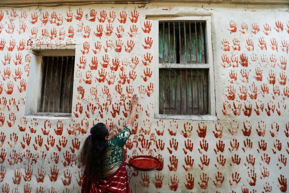 A lady making red handprints on the wall, on the first day of Navratri during which devotees worship the Hindu goddess Durga, in Ahmedabad, India, on Oct 3, 2024.