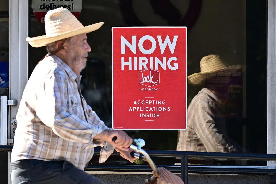 (FILES) A cyclist rides past a "Now Hiring" sign posted on a business storefront in San Gabriel, California on August 21, 2024. US hiring picked up pace in August while the jobless rate crept down, according to government data released September 6, 2024, paving the way towards the start of central bank rate cuts this month. (Photo by Frederic J. BROWN / AFP)