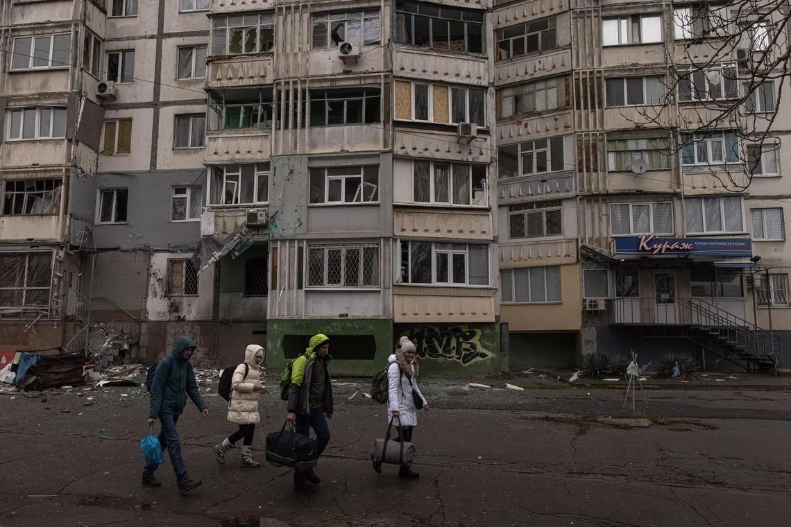 People with their luggage walk past a damaged residential building after the recent Russian attack in Kherson, on Nov 25, 2022.