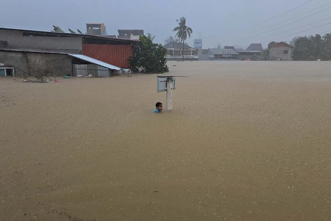 A man clinging to a street sign on a flooded street after being swept there while going out to get food supplies in Hat Yai district, which has been affected by heavy rainfall that has hit 10 provinces in southern Thailand and killed several people, in Songkhla province, Thailand, Nov 24, 2025. 