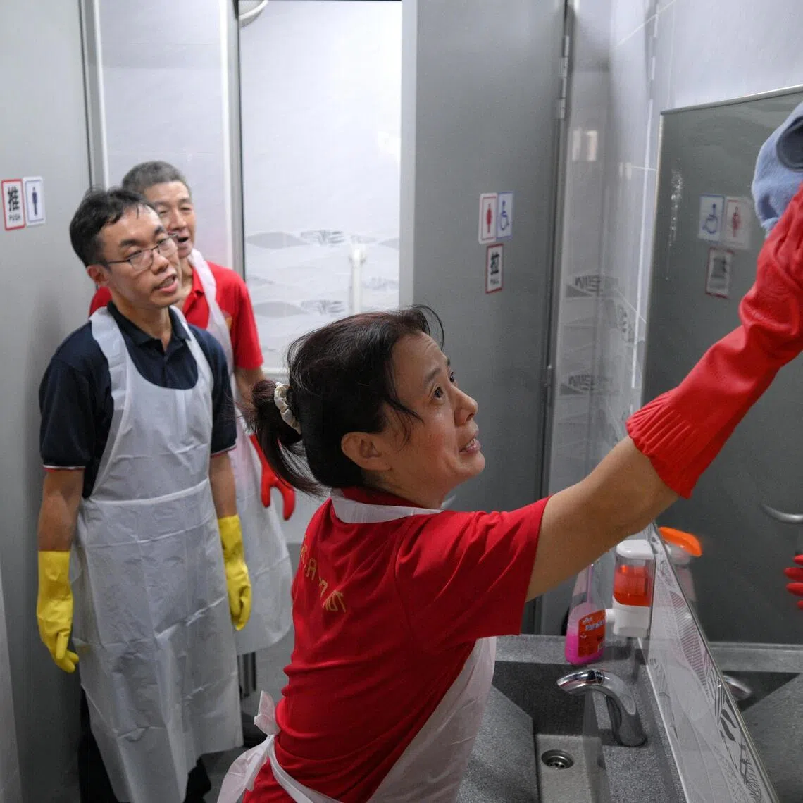 Cleaners (in red), supervised by a trainer (in blue) from Ascendo Academy, clean a mirror at the common wash basin of the newly renovated toilet at Rong Fa Coffeeshop at Clementi West Street 2 pictured on May 15, 2026. (Pls note, female cleaner and male trainer did not want to be named)
