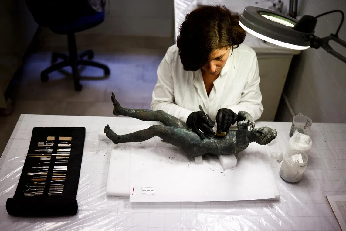 Restorer Laura Rivaroli works on a bronze statue of Apollo in the pose of an archer is laid out on a table for restoration, after it was discovered and pulled out from the muddy ruins of an ancient spa in San Casciano dei Bagni, a hilltop village in southern Tuscany still home to popular thermal baths, in Grosseto, Italy, May 29, 2023. REUTERS/Guglielmo Mangiapane