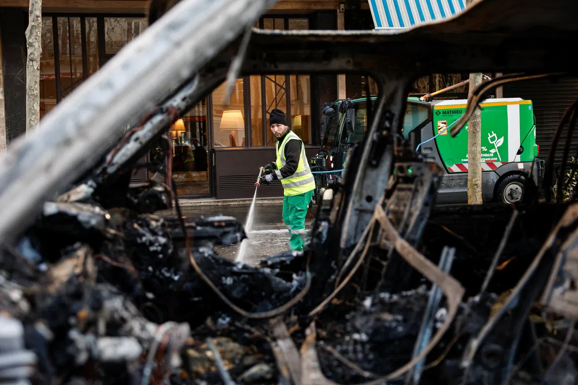 A municipal worker, seen through a burnt-out car, cleans a street on Oct 18, a day after the protests.