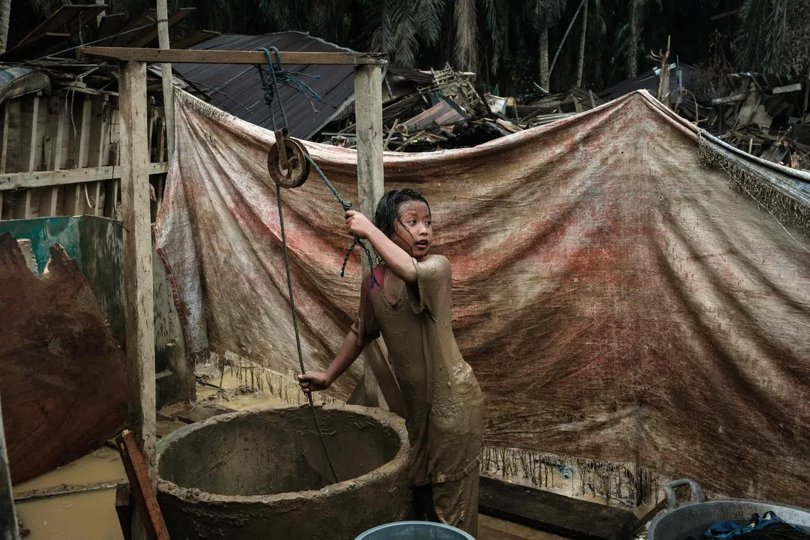 Baiti Arafah pulling up a bucket of water from a well to clean herself after playing in a muddy puddle in Babo, Aceh Tamiang, Indonesia on Dec 15, 2025, following a flash flood. 