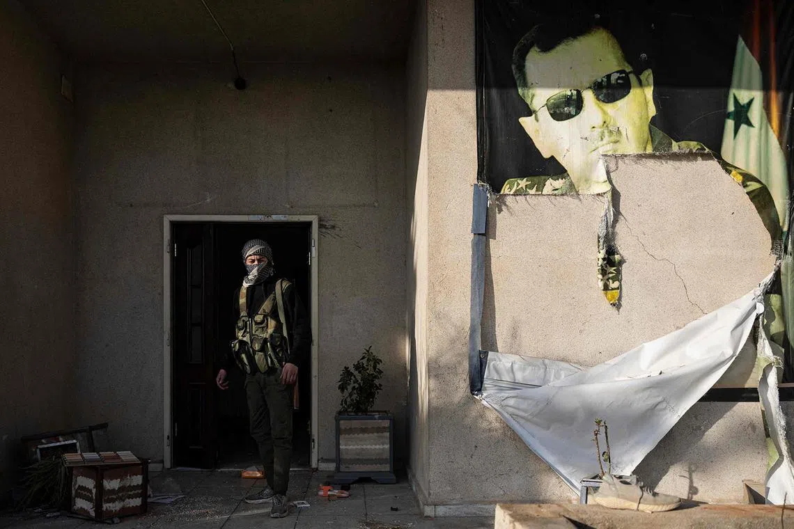 TOPSHOT - A rebel fighter walks past a defaced picture of toppled Syrian president Bashar al-Assad in a military base in the capital Damascus on December 26, 2024. (Photo by Sameer Al-DOUMY / AFP)