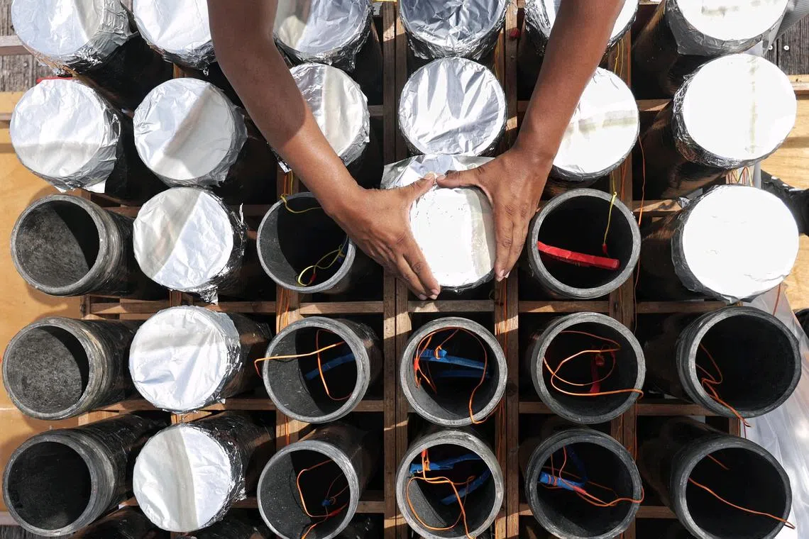 A worker using aluminium foils to seal the opening of tubes that have been loaded with shells during the preparation process on a pontoon at Kallang Basin on Dec 27, 2024. Fireworks preparations at Singapore Sports Hub for the Let's Celebrate New Year's Eve countdown.