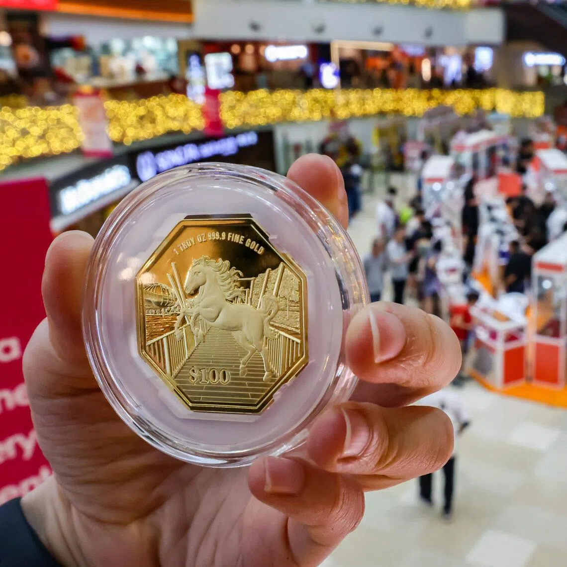 A close-up of the Singapore Year of the Horse 1 troy oz 999.9 fine gold coin juxtaposed against the Singapore Mint Lunar Fair at Chinatown Point Atrium on its opening day on Jan 1, 2026. The fair, which runs from Jan 1 to 11, offers the public a first look at newly issued Lunar New Year-themed coins, gifts and collectibles. Jan 1 also marks the first day of issuance of the Singapore Year of the Horse coins. Featuring the horse, the seventh animal in the Chinese zodiac, the coin design is set against Punggol Waterway Park, part of the North Eastern Riverine Loop linking four parks. The series comprises 10 versions across different face values, formats, metallic compositions and relief treatments. 