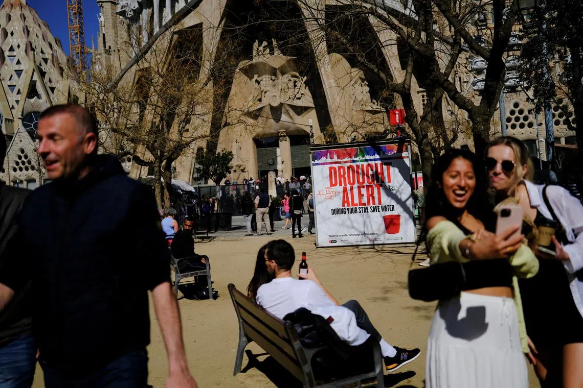 Tourists are seen next to a sign at Sagrada Familia Basilica alerting them of severe drought in Spain's northeastern region and urging them to save water due to low reservoir levels, as Catalonia declares state of emergency, in Barcelona, Spain, March 14, 2024. REUTERS/Nacho Doce