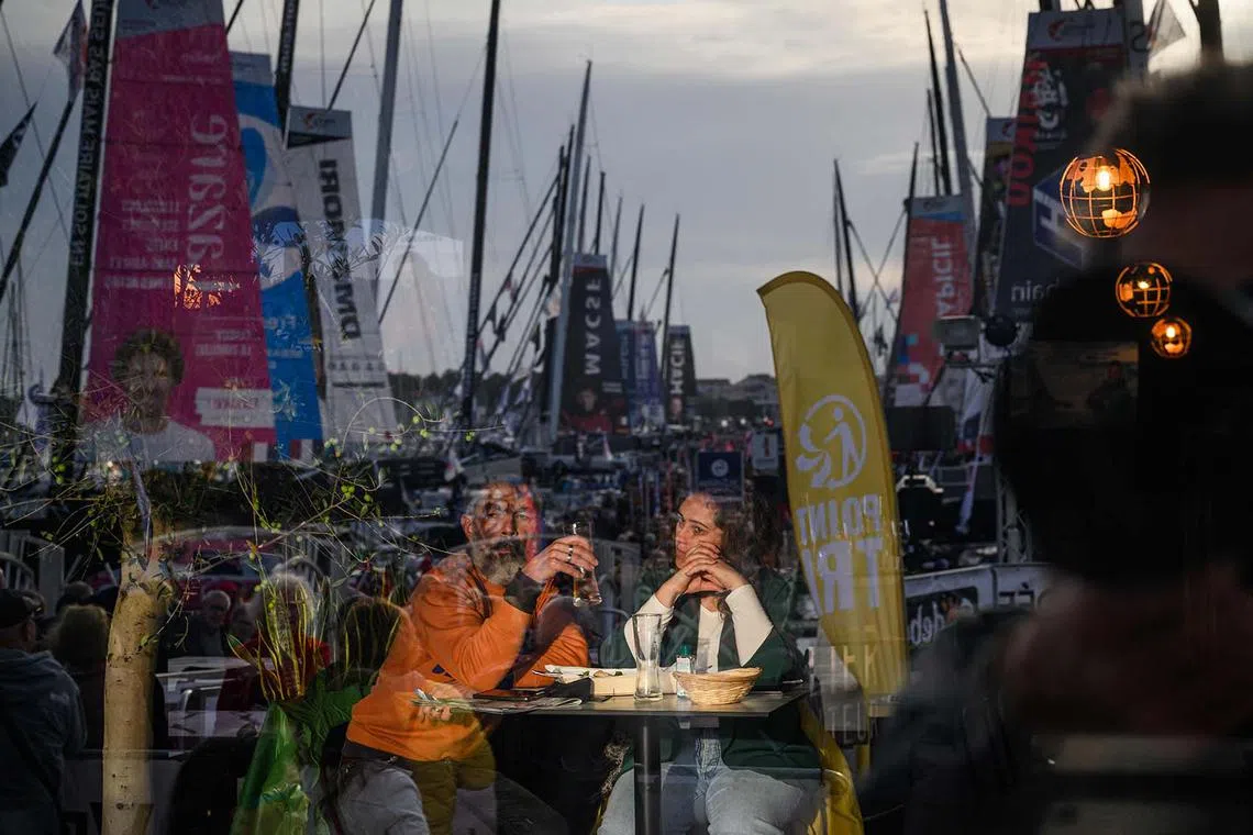 Two people look at visitors walking at the starting site of the 10th edition of the Vendee Globe around the world monohull solo sailing race, on the Vendee Globe village in Les Sables-d'Olonne, western France on November 4, 2024. With just a few days to go before the start of the 10th Vendee Globe, on November 10, 2024, everything is almost ready on the pontoons in Les Sables-d'Olonne, after a sad and silent start of the 2020 edition due to lockdown. (Photo by Loic VENANCE / AFP)