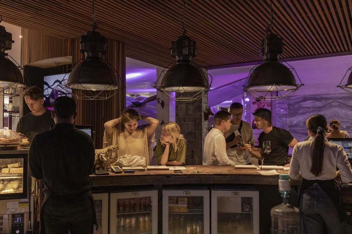 — EMBARGO: NO ELECTRONIC DISTRIBUTION, WEB POSTING OR STREET SALES BEFORE 3:01 A.M. ET ON SUNDAY, JAN. 15, 2023. NO EXCEPTIONS FOR ANY REASONS —Customers wait to order at a café at Parq Ubud in Bali, Indonesia, which has become a popular place to live and work for the Russians and Ukrainians who have fled, Dec. 12, 2022. Thousands of Russians and Ukrainians have fled their homelands for Bali. — But even in a tropical paradise, the war is ever-present. (Nyimas Laula/The New York Times)