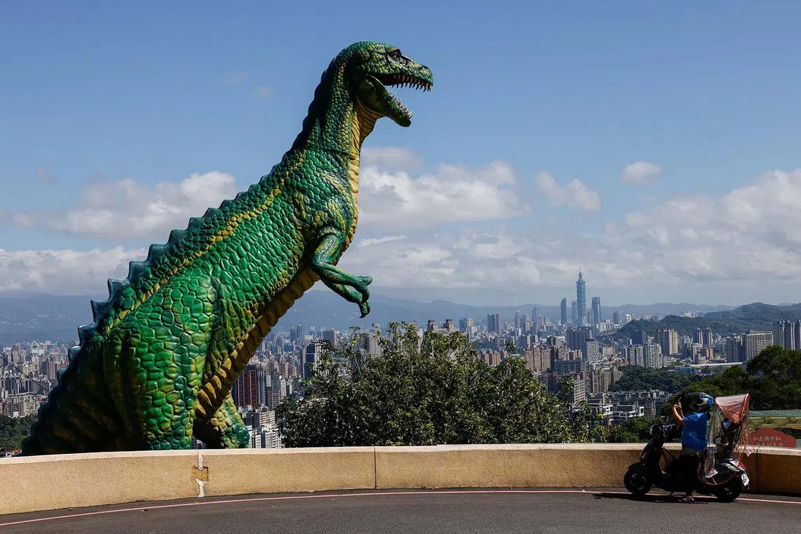 A woman takes a photo of a dinosaur statue, with Taipei 101 in the background, in Taipei, Taiwan October 15, 2024 REUTERS/Tyrone Siu