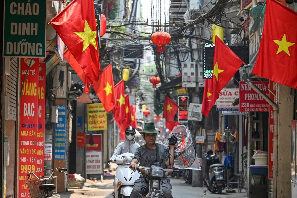 A man carries a fan on a hot day while riding a motorbike along a street lined with Vietnamese national flags in Hanoi on April 30, 2024. Extreme heat is scorching parts of South and Southeast Asia, prompting health warnings from authorities as high temperatures are recorded across the region. (Photo by Nhac NGUYEN / AFP)
