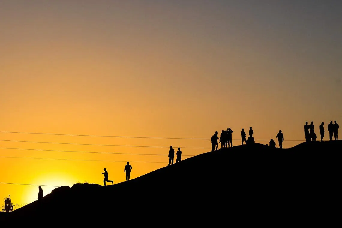 TOPSHOT - Palestinians are silhouetted against the setting sun as they stand on a hill on the Gaza-Egypt border in Rafah, on the southern Gaza Strip, on December 26, 2023, amid the ongoing battles between Israel and the militant group Hamas. (Photo by MAHMUD HAMS / AFP)