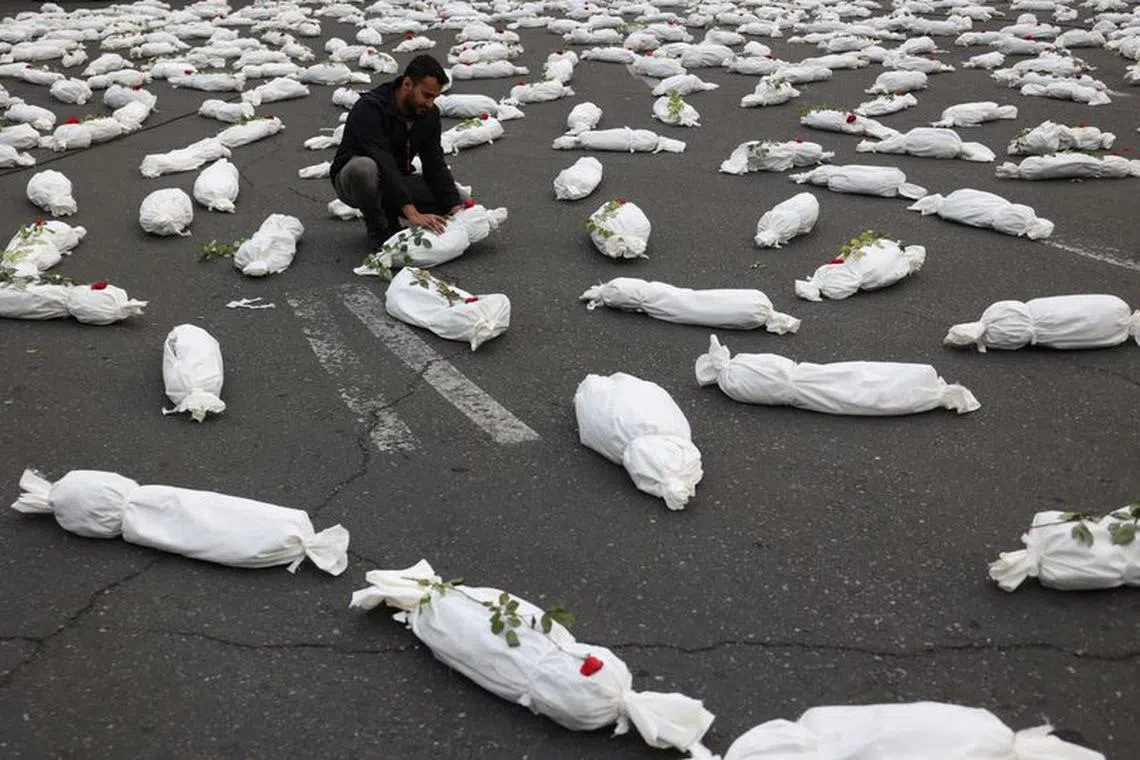 An Iranian man sits next to the symbolic shrouds of Gaza children's dead bodies during a gesture in a street in Tehran, Iran November 13, 2023. Majid Asgaripour/WANA (West Asia News Agency) via REUTERS/ File Photo