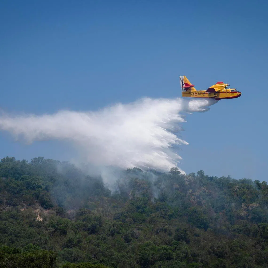 A firefighting plane releasing water over a forest fire near a residential area in Calonge in Catalonia, Spain, on July 4.